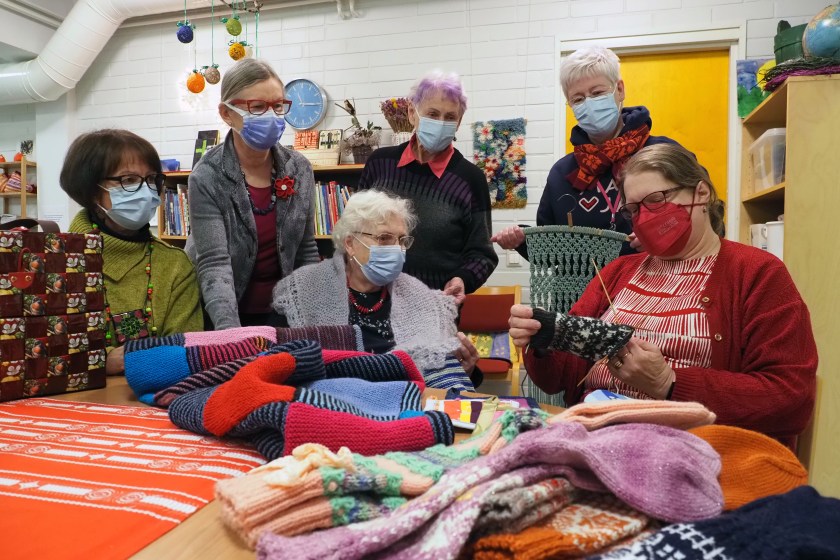 Kuusi naista käsitöiden kanssa pöydän ympärillä.