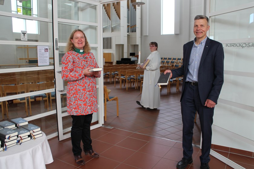 Leena Mgaya ja Pekka Auvinen seisovat Noljakan kirkkosalin ovella, Emilia Heikkinen kävelee kirkkosalissa alba päällä ja kynttilä kädessä.