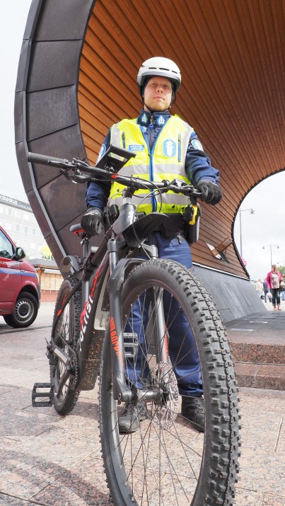 Polkupyöräpoliisi seisoo pyörän kanssa Joensuun torilavan edessä.