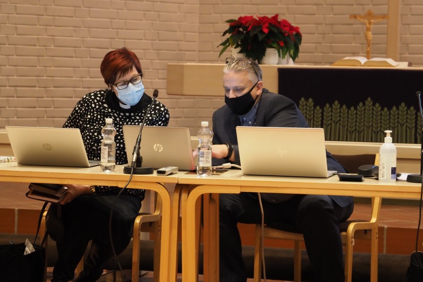 Yhteisen kirkkoneuvoston puheenjohtaja Tiina Reinikainen ja Joensuun seurakuntayhtymän hallintojohtaja Tommi Mäki istuvat tietokoneiden ääressä ja tutkivat papereita. Molemmilla on maskit kasvoillaan.