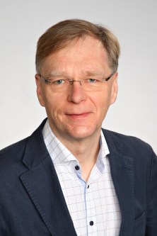 Silmälasipäinen, ruskeatukkainen mies katsoo kameraan päin.