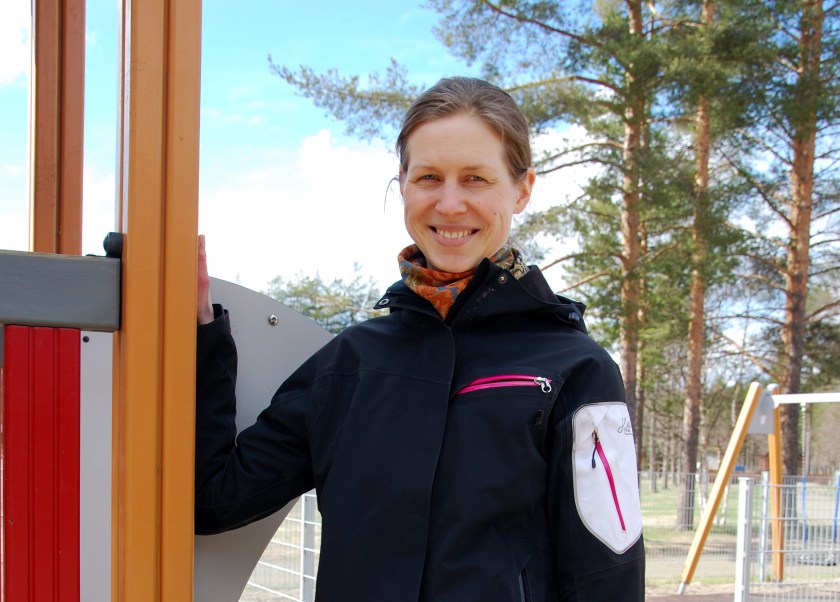 Johanna Ojala seisoo päiväkodin pihalla lasten leikkitelineen luona hynyillen.