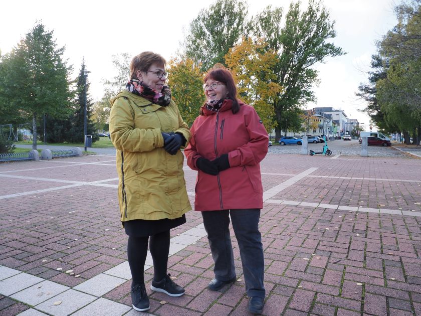 Kaksi hymyilevää naista juttelee kadulla.