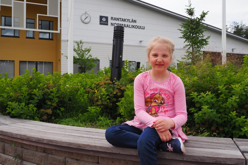 Hymyilevä, vaaleatukkainen pieni tyttö katsoo kameraan päin.