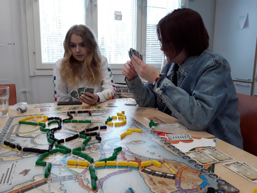 Nuoret pelaavat lautapeliä pöydän ääressä.