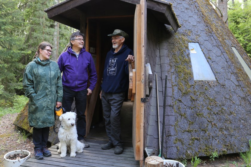 Kolme ihmistä ja koira kodan oviaukolla.