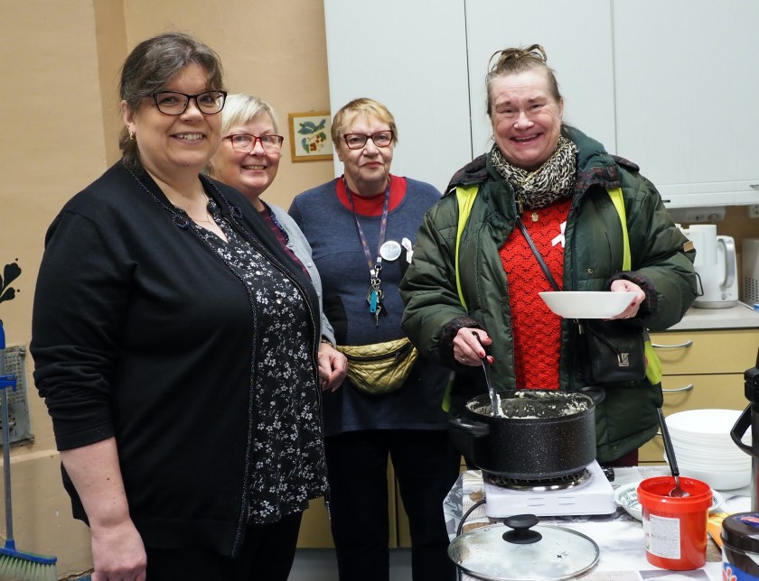 Diakoniatyöntekijä Auli Pehkonen, tarjoiluissa avustava Olga Yufa sekä Utran asukasyhdistyksen emäntä Aune Timoskainen seisovat tarjoilupöydän ääressä, Eija Nieminen ottaa kattilasta puuroa lautaselle.