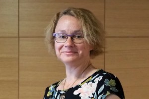 hymyilevä nainen puisen paneeliseinän edessä