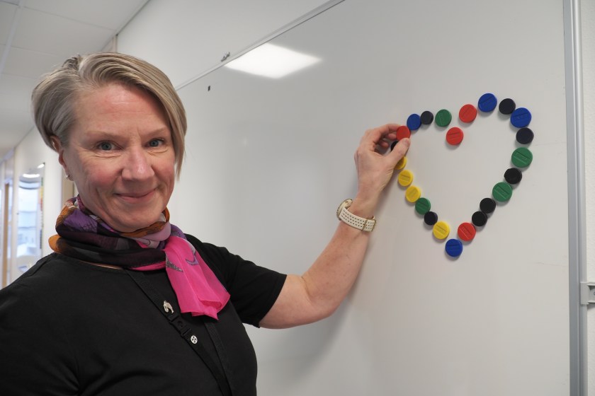 Vaalea nainen taululle tekemänsä värikkään sydämen äärellä.