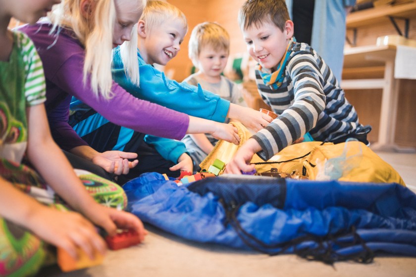 Viisi lasta leikkimässä iloisesti yhdessä sisätiloissa.