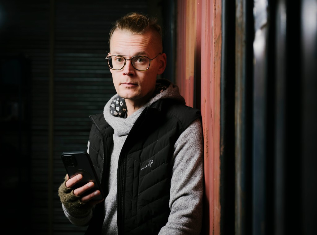 Silmälasipäinen mies kännykkä kädessään.