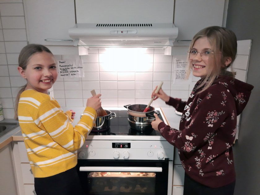 Kaksi tyttöä kokkaa sähköhellan äärellä.