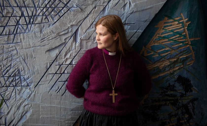 Naispiispa seisoo harmaan seinän vierellä.