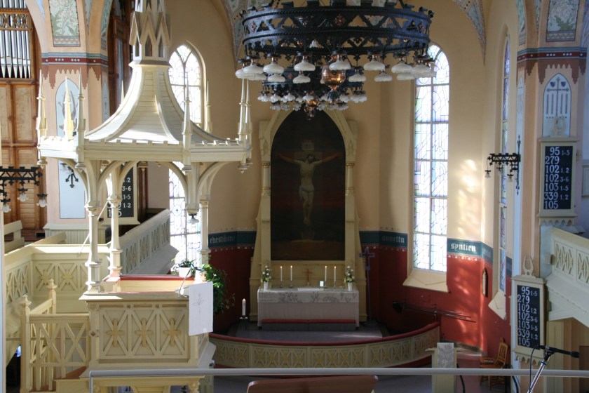 Joensuun kirkon alttari ja saarnastuoli auringon paistaessa ikkunoista sisään.