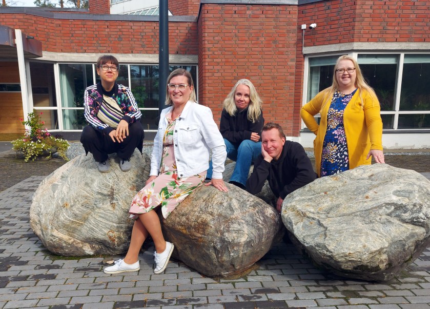 Joukko nuorisotyöntekijöitä istuskelee Rantakylän kirkon edessä olevilla isoilla kivillä ja hymyilee kameralle.