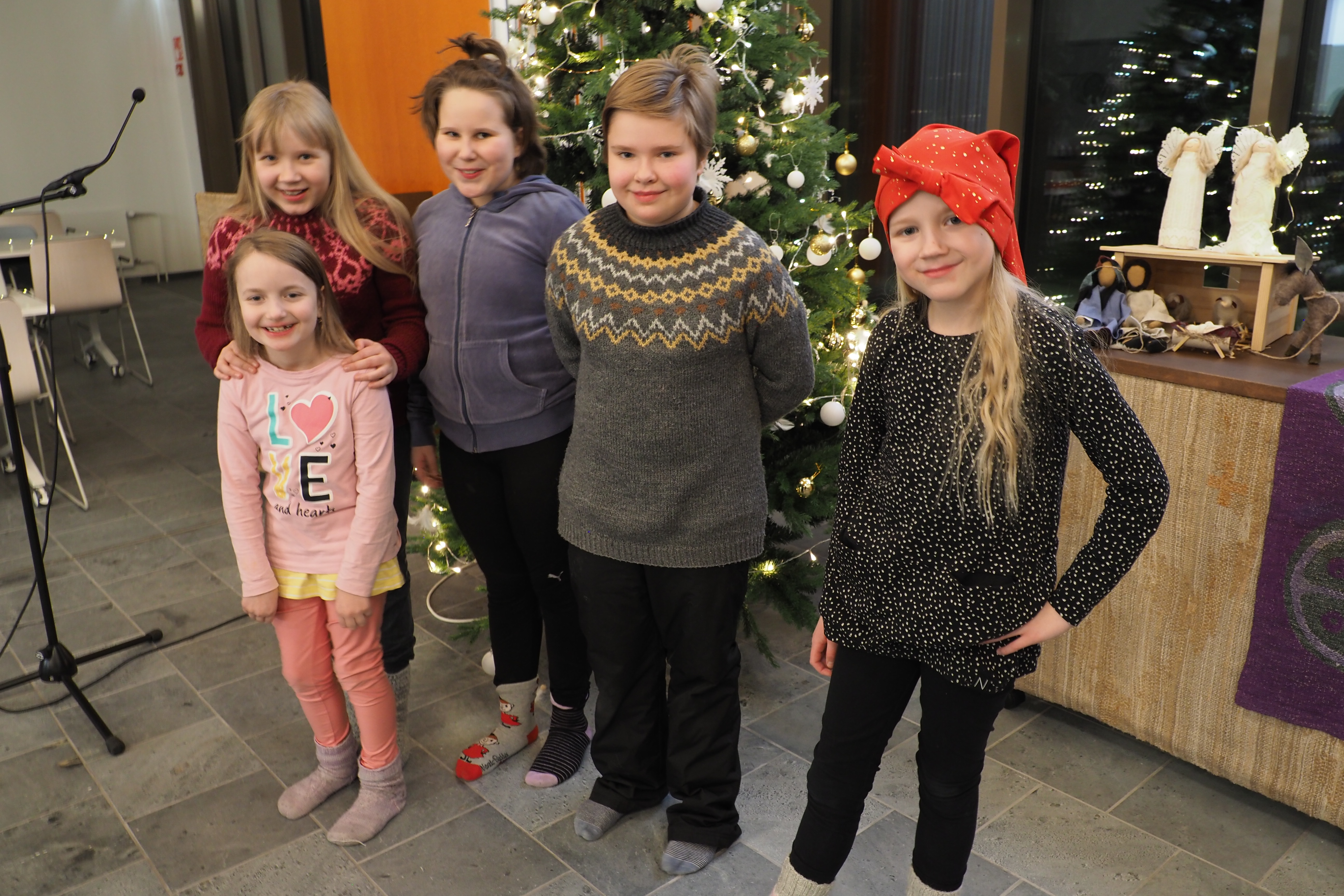 Viisi lapsikuoron lasta joulukuusen äärellä.