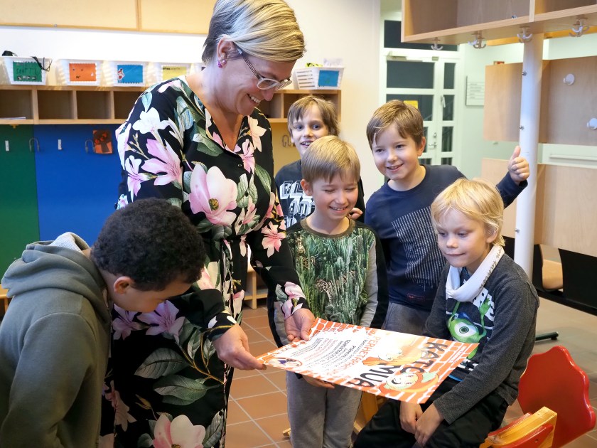 Nuorisotyönohjaaja Noora Kähkönen pitää kädessään Kato mua -tapahtuman julistetta. Viisi alakouluikäistä poikaa ovat kokoontuneet katsomaan julistetta.